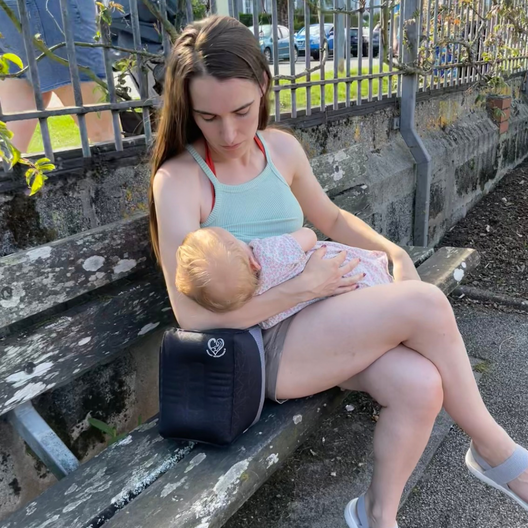 Mother breastfeeding her child in public on a bench using a portable feeding pillow for support